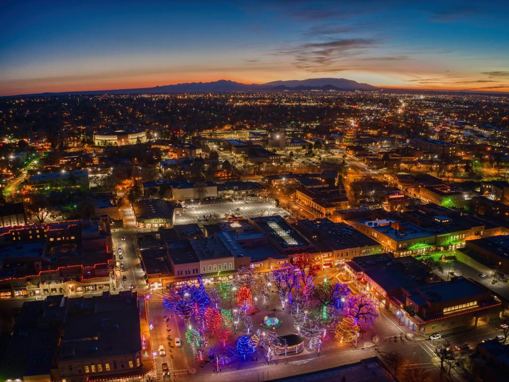 Aerial cityscape showing the lights of low rise buildings with brightly colored Christmas trees in the Plaza in the foreground
