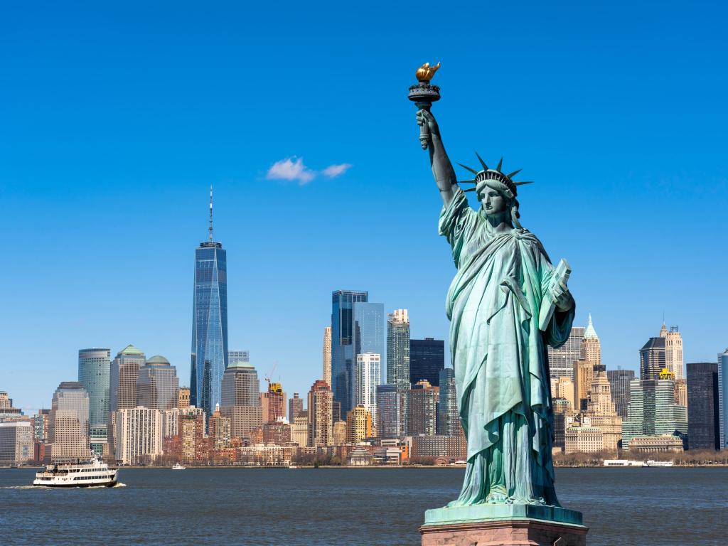 The Statue of Liberty over the silhouette of New York cityscape river side in lower Manhattan.