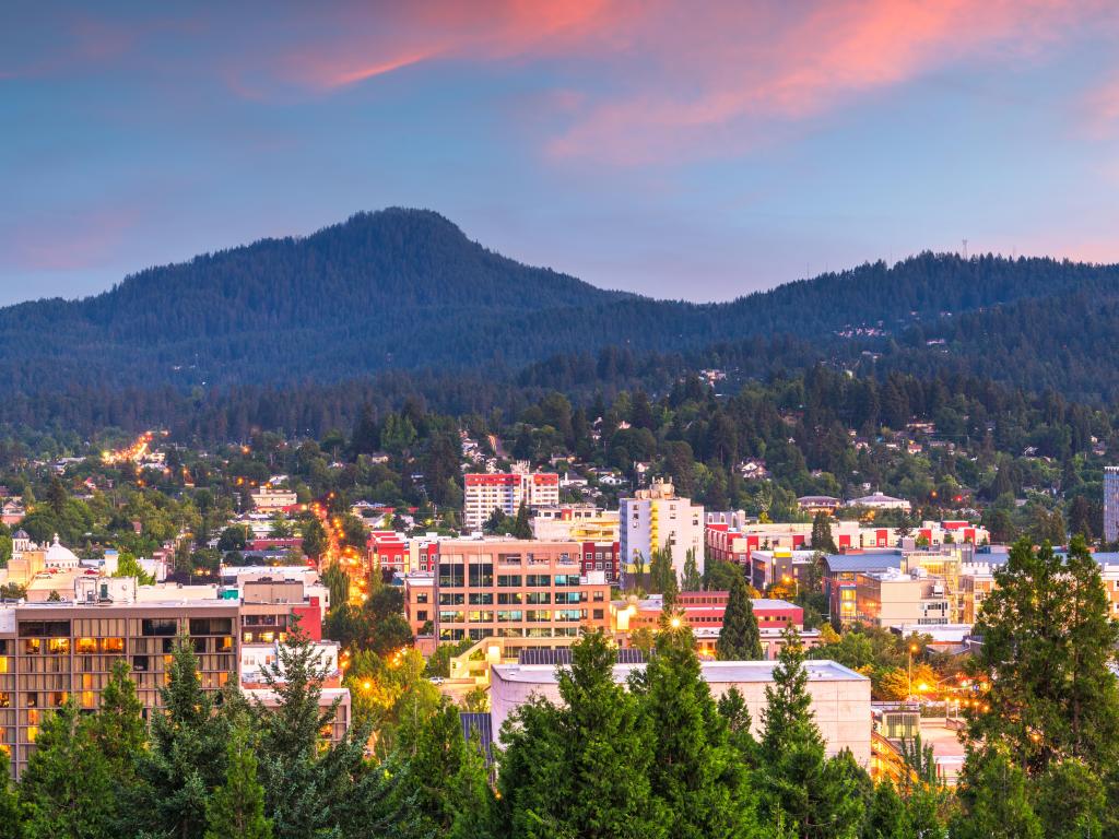 Eugene, Oregon, USA with the downtown cityscape and mountains at dusk and tree-covered mountains in the distance.
