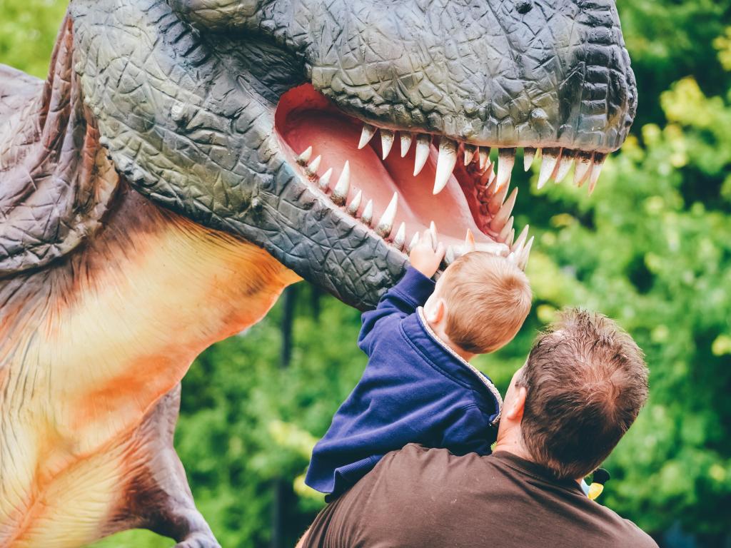 A young child touching a dinosaur sculpture at the amusement park