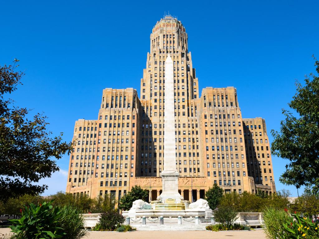 Buffalo City Hall, Buffalo, USA with trees and plants in the foreground and the iconic building against a bright blue background.