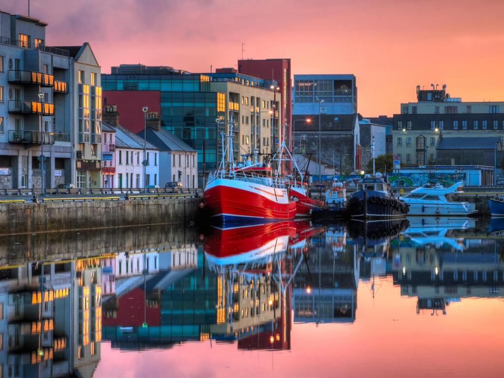 Galway Dock, Ireland with a morning view on row of buildings and fishing boats in Galway Dock with sky reflected in the water.
