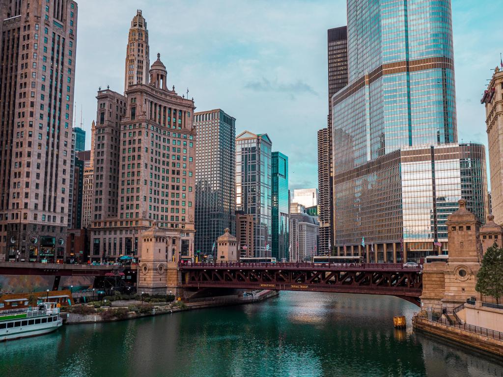 Bridge across river with skyscrapers in the background, with pale blue cloudy sky