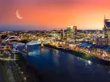 Nashville, Tennessee with the city in the background and the river in the foreground at night with the moon visible in a red sky.