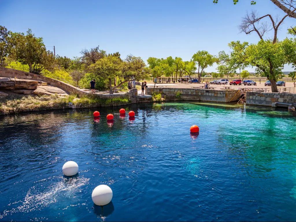Blue Hole, Santa Rosa, New Mexico, USA with the deep pool with clear blue water in the foreground, and a platform with trees in the background. 