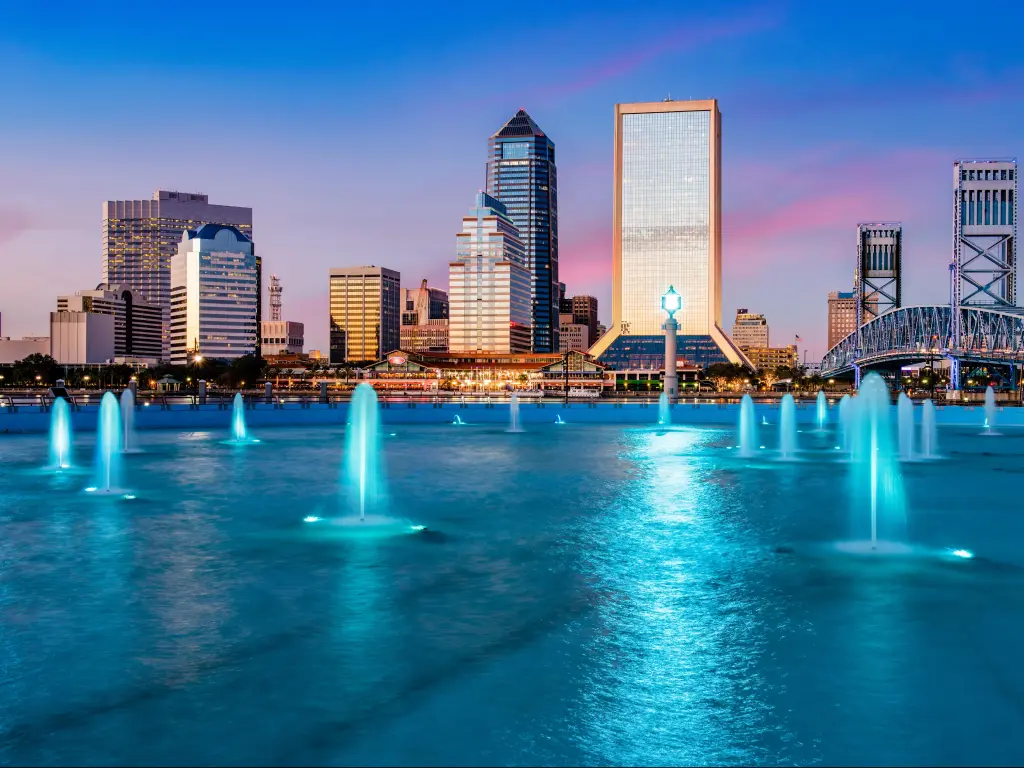 Jacksonville, Florida, USA wit the city skyline in the background and the fountain lit up at night in the foreground.