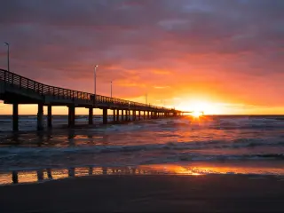Corpus Christi, Texas, USA with the Bob Hall Pier on Padre Island at sunset with the sun low against the sea and beach in the foreground.