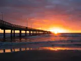 Corpus Christi, Texas, USA with the Bob Hall Pier on Padre Island at sunset with the sun low against the sea and beach in the foreground.
