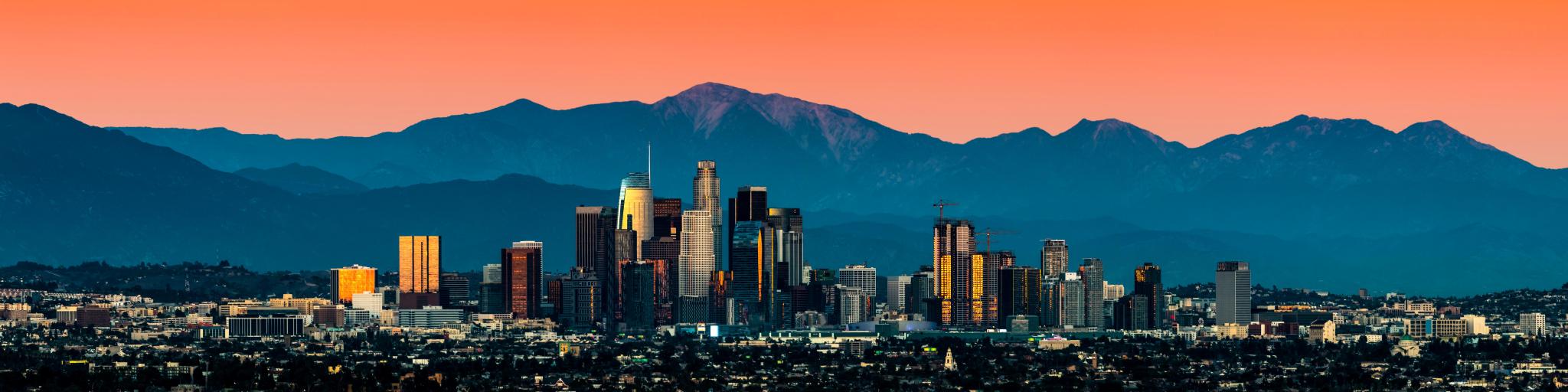 Panoramic view of Los Angeles skyline with mountains in the background and vibrant orange sunset