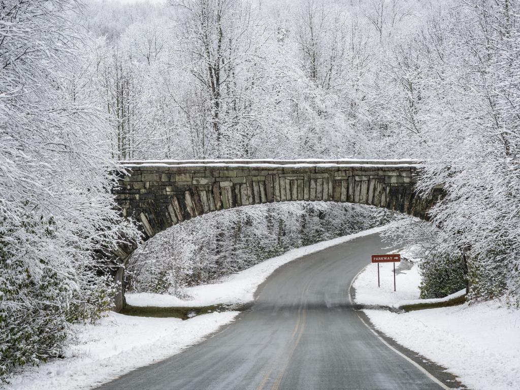 Icy road through Snow covered forest with a small brick bridge over the road