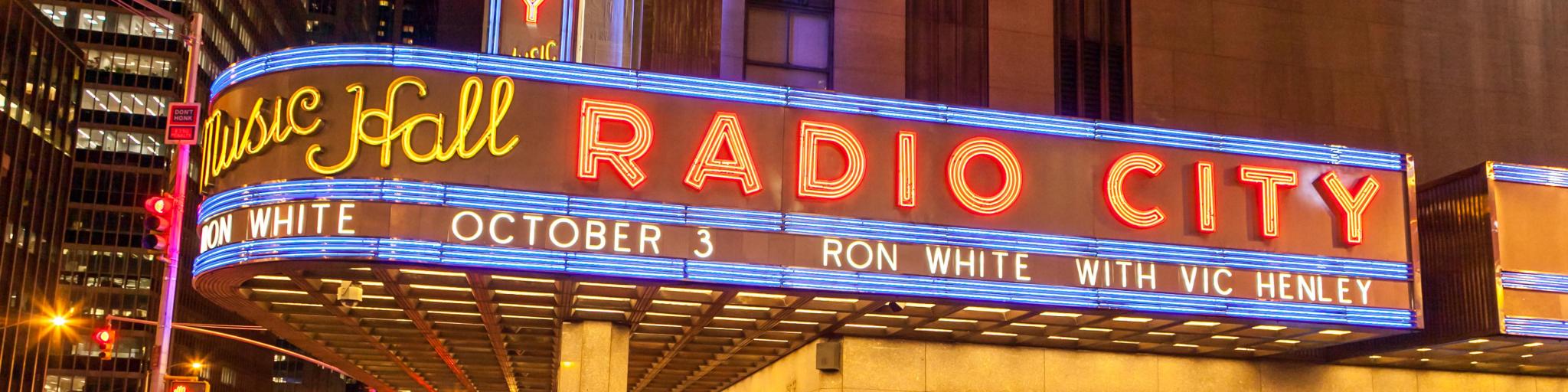 Lit up sign of the Radio City Music Hall, New York, with people walking past