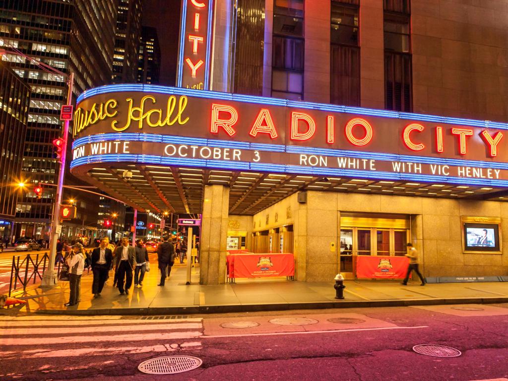 Lit up sign of the Radio City Music Hall, New York, with people walking past