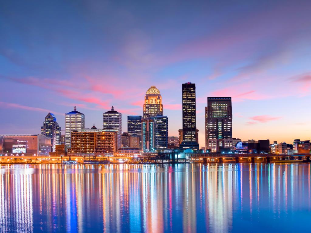 Louisville, KY skyline at sunset, with lights reflecting on the water below