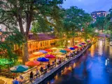 San Antonio, Texas, USA cityscape at the River Walk as the evening falls. There are colorful umbrellas on the riverside, with tables.