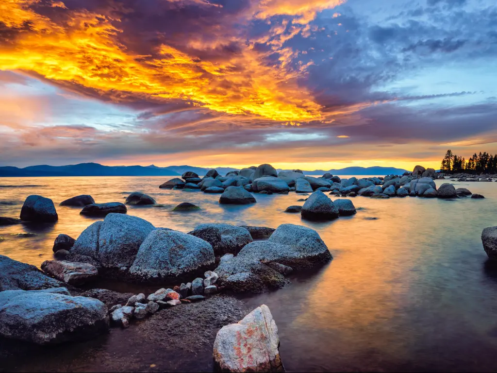 Lake Tahoe, Nevada and California, USA taken at Zephyr Cove at a dramatic sunset with calm waters surrounding large rocks and a yellow sky.