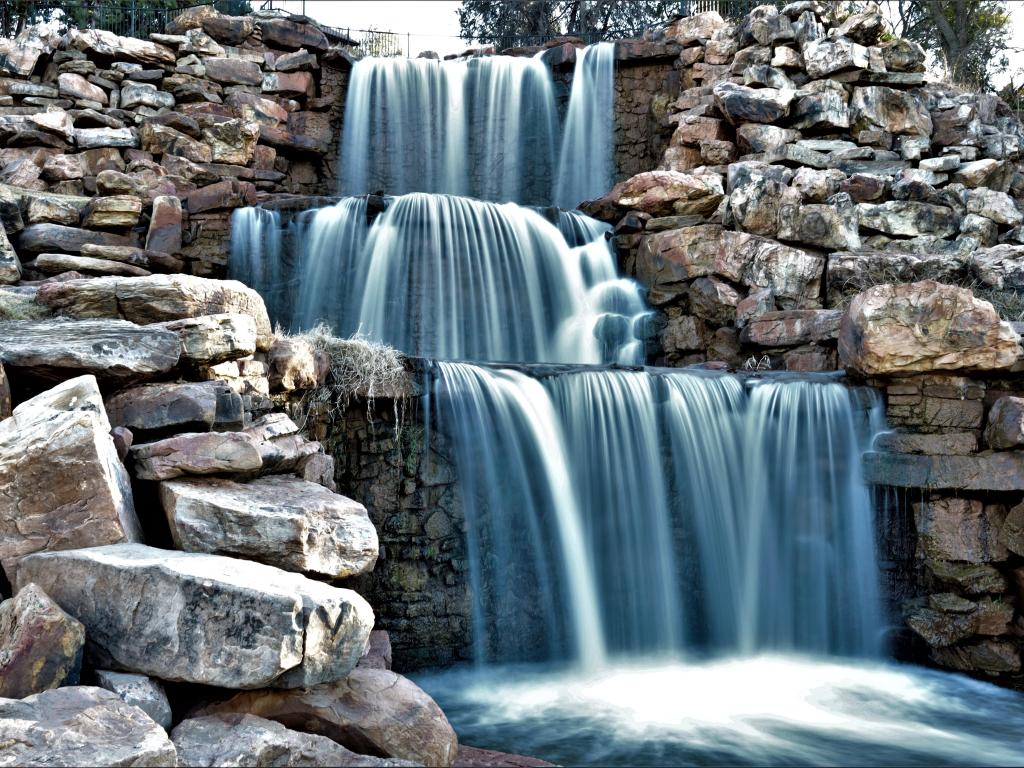 Photo of a stunning manmade waterfall surrounded by small boulders in Wichita Falls Texas, photo taken with long exposure