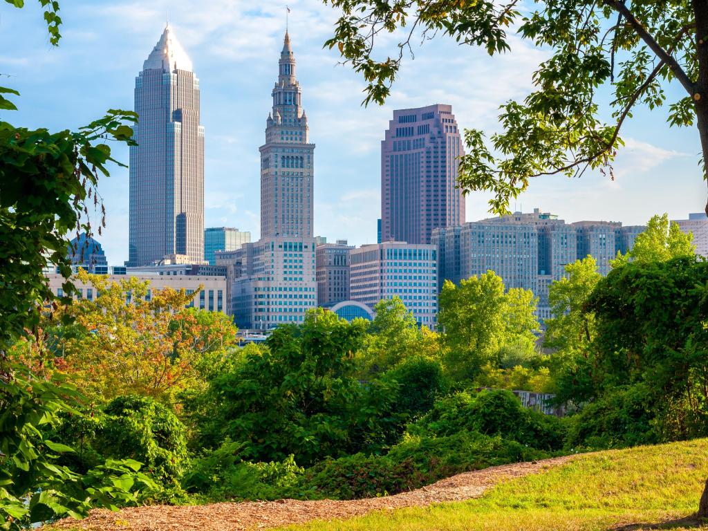 Cleveland, Ohio with a view of downtown in the distance from a small park in morning light, framed by trees and grass in the foreground.