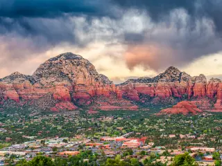 Sedona, Arizona, USA with the downtown cityscape and mountains in the distance against a cloudy sky.