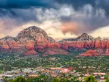 Sedona, Arizona, USA with the downtown cityscape and mountains in the distance against a cloudy sky.