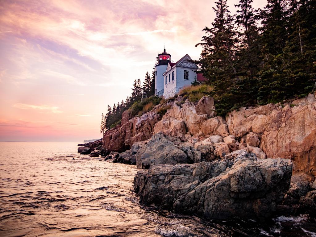 Bass Harbor Lighthouse, Acadia National Park, USA taken at sunset with the famous landmark on Mount Desert Island, rugged rock cliffs and the sea in the foreground.