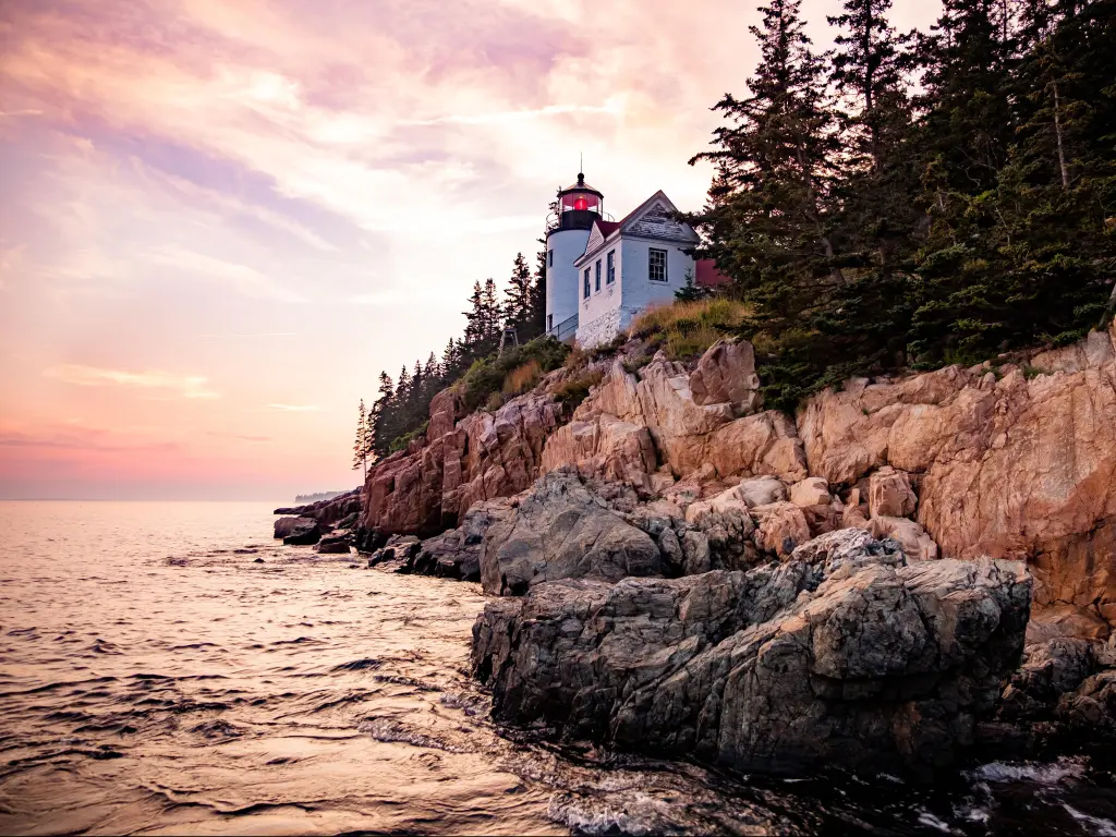 Bass Harbor Lighthouse, Acadia National Park, USA taken at sunset with the famous landmark on Mount Desert Island, rugged rock cliffs and the sea in the foreground.