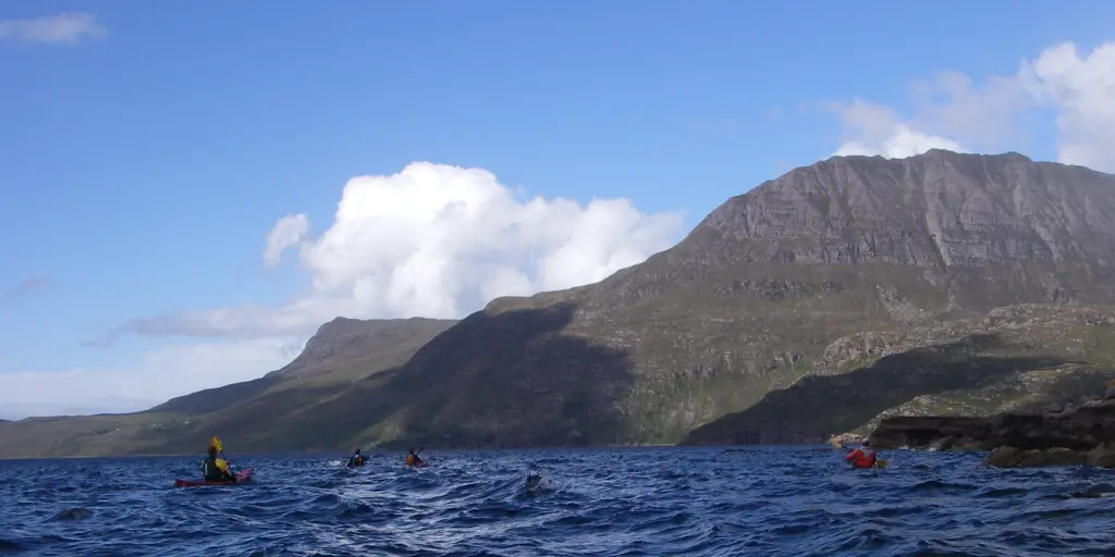 The tip of a kayak in the water, with other kayaks and mountains in the background