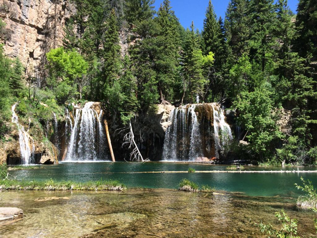 Hanging Lake, Glenwood Springs, Colorado, USA with trees and cliffs in the distance and a waterfall with lake in the foreground.