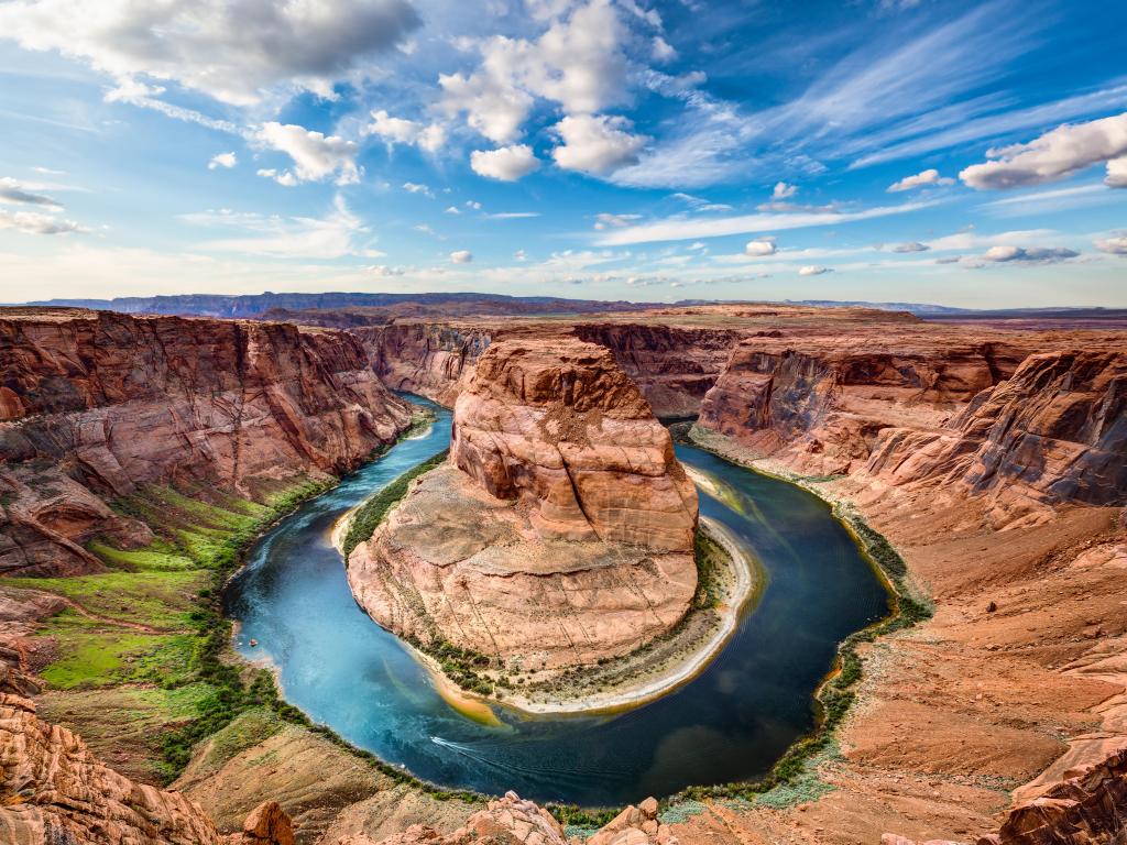 View down into a valley with a u-shaped bend in the river. Brown rocks and blue sky with white clouds.