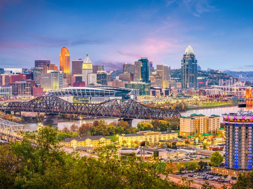 Cincinnati, Ohio, USA with the city skyline and bridge in the distance and trees in the foreground taken at dusk.