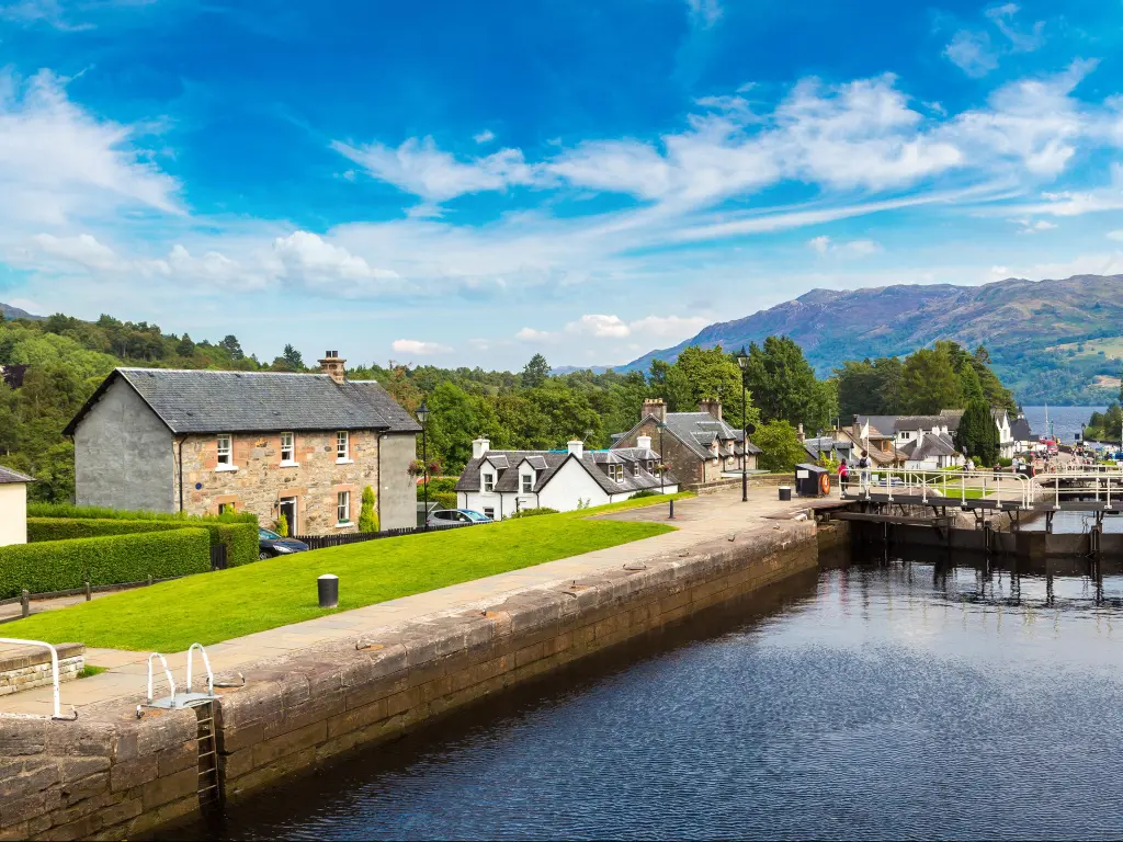 Fort Augustus, Scotland, United Kingdom with a water gateway surrounding by buildings and mountains in the distance on a sunny day.