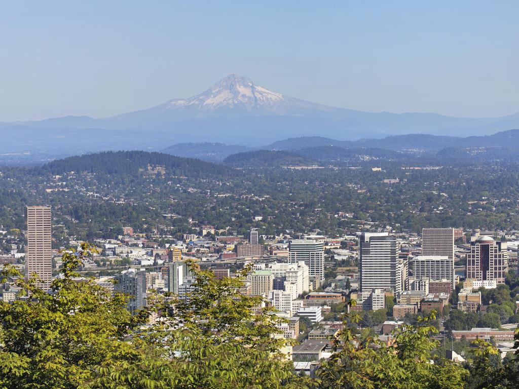 Portland, Oregon, USA with the downtown cityscape and landscape with Mount Hood and trees in the foreground taken on a sunny day.