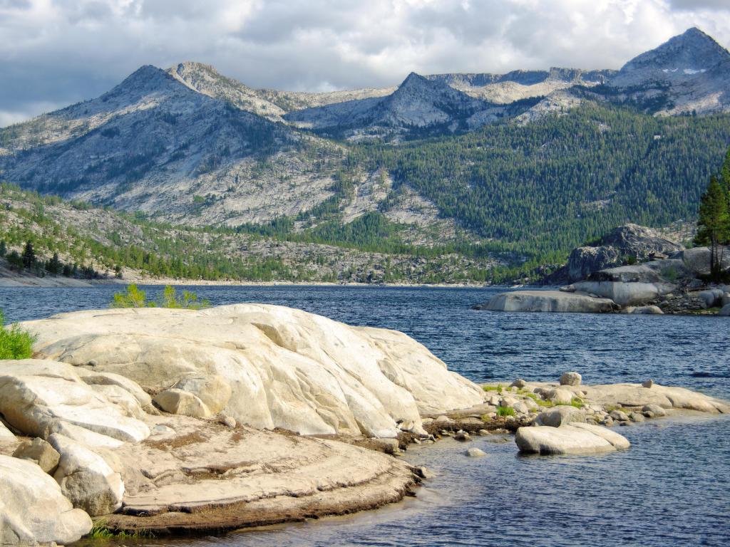 Large rocks at the shore of Florence Lake, with tall, pine dotted mountains in the background on a cloudy day