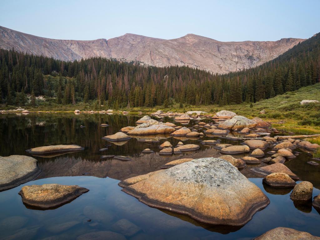 Mount Evans, Colorado with rocks in the beautiful lake in the foreground and Mount Evans and a forest in the background. 