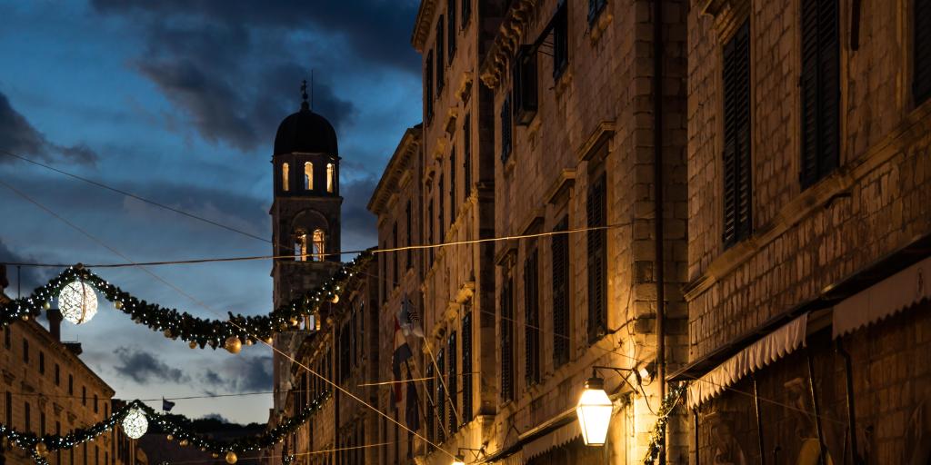 Stradun old street with bell tower decorated with shining Christmas lights and ornaments at dawn, Dubrovnik, Croatia