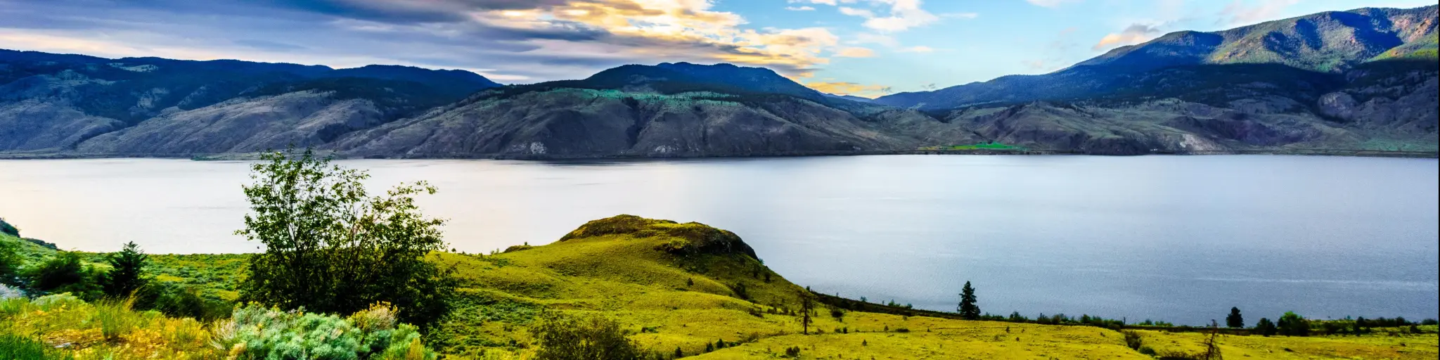 Kamloops Lake, Trans Canada Highway, British Columbia, Canada at sunset with green land in the foreground, a lake and mountains in the distance. 