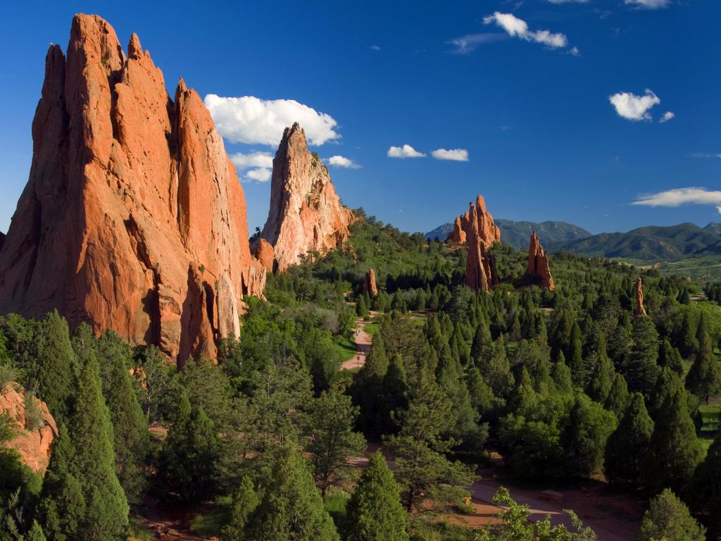 Panoramic shot of Garden of the Gods, Colorado Springs, with lush greenery in the foreground on a sunny day with blue skies above