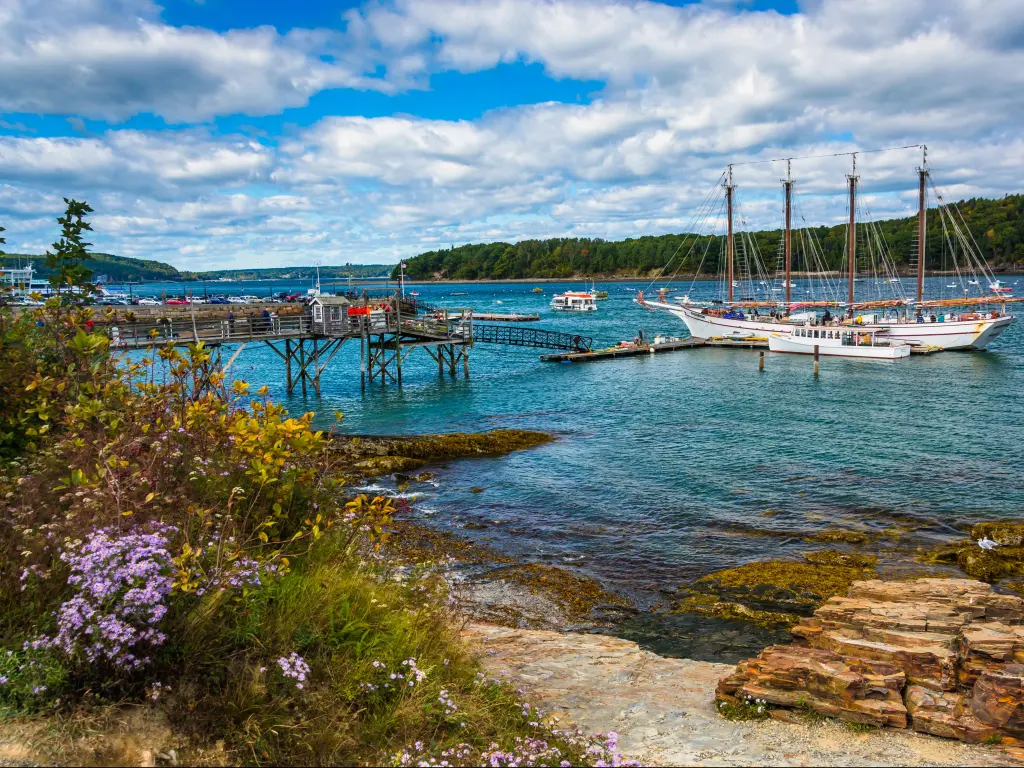 Bar Harbor, Maine, USA taken at the rocky coast and view of boats in the harbor on a sunny day.