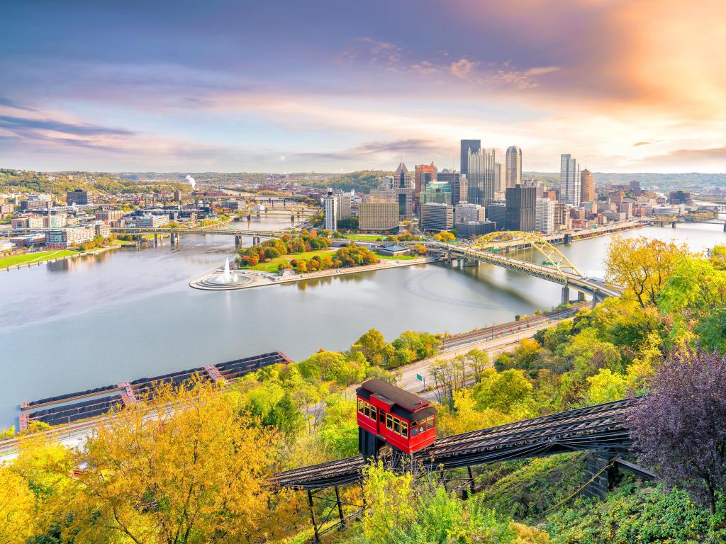 View across the river from a high vantage point towards the downtown area where two rivers meet, showing high rise buildings. In the foreground, red funicular car travels up the hill.