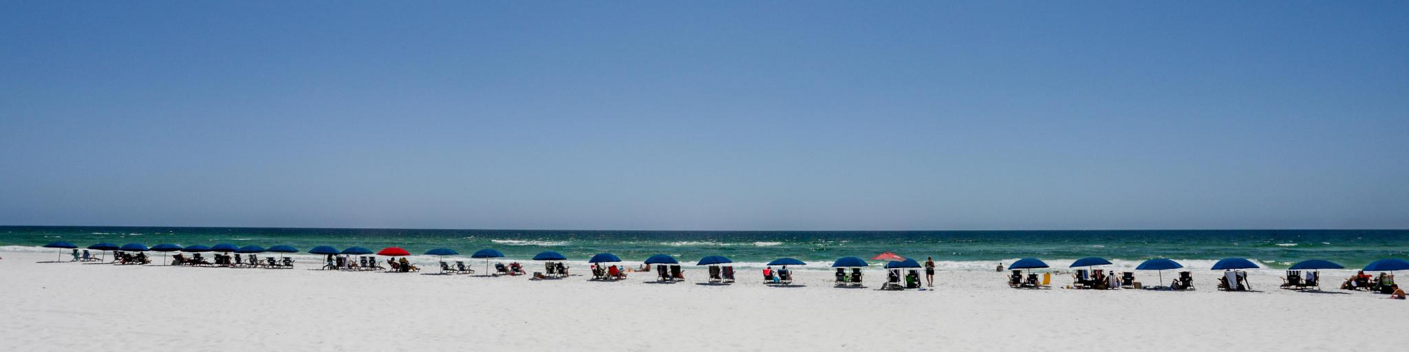 A line of people on sun loungers with umbrellas along a white sandy beach in Destin, Florida