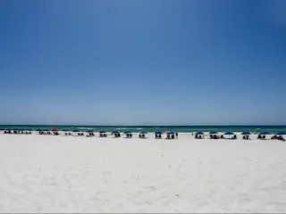 A line of people on sun loungers with umbrellas along a white sandy beach in Destin, Florida