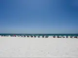 A line of people on sun loungers with umbrellas along a white sandy beach in Destin, Florida