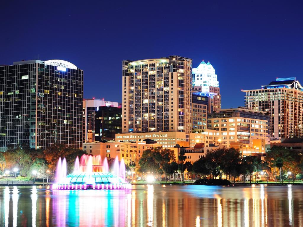 Orlando, Florida, USA downtown skyline panorama over Lake Eola at night with urban skyscrapers, fountain and clear sky.