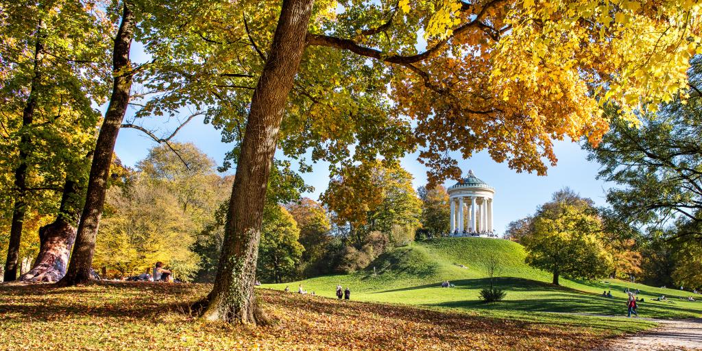 The English Garden Munich on an Autumn day, with the Greek Temple shown sitting on a grassy hill and lots of colourful leaves and trees