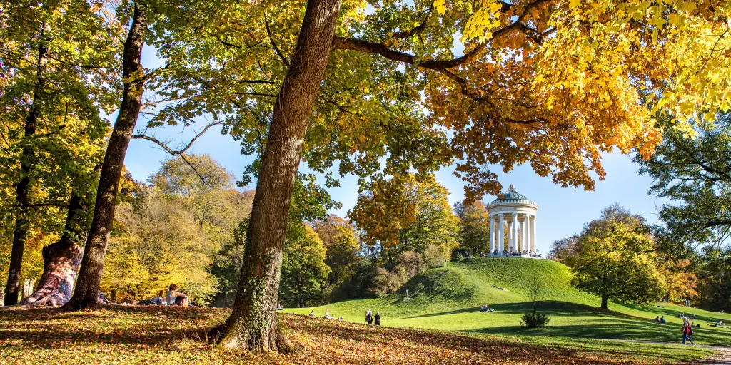 The English Garden Munich on an Autumn day, with the Greek Temple shown sitting on a grassy hill and lots of colourful leaves and trees