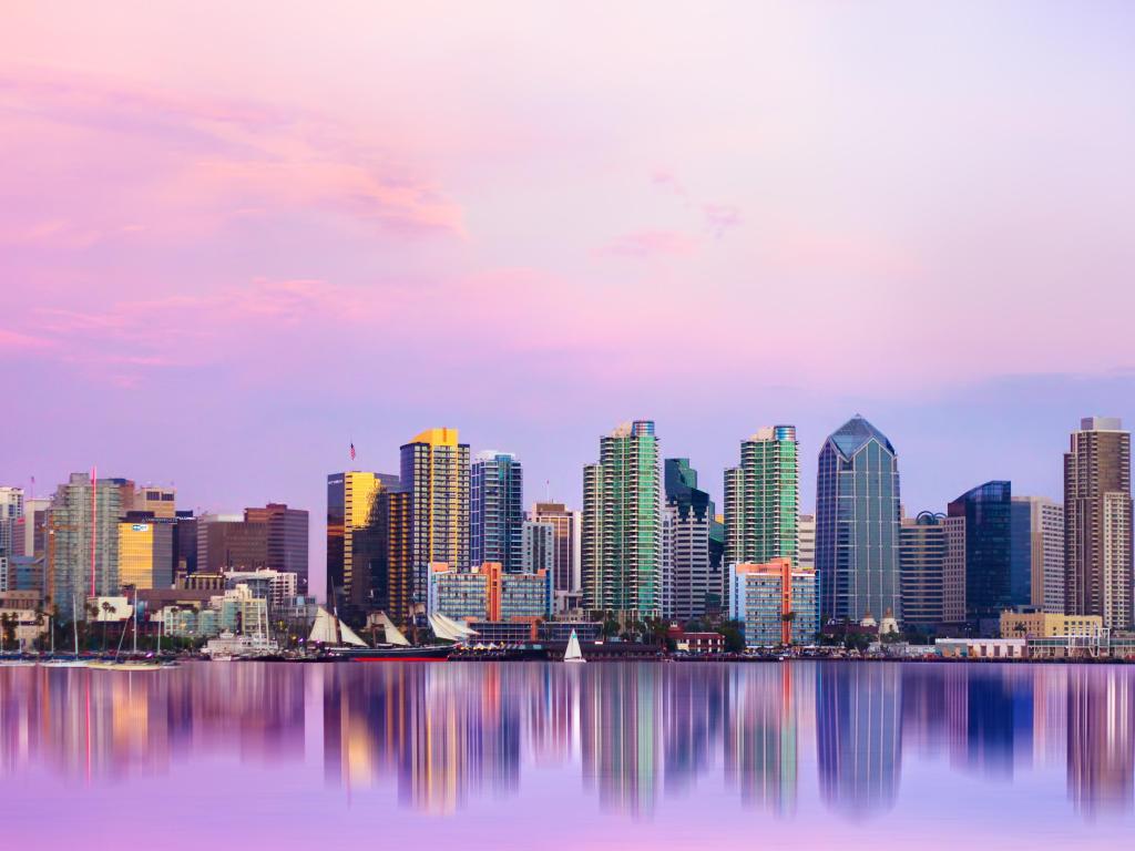 High rise buildings viewed across lake at sunset with pink and blue sky reflected in still water
