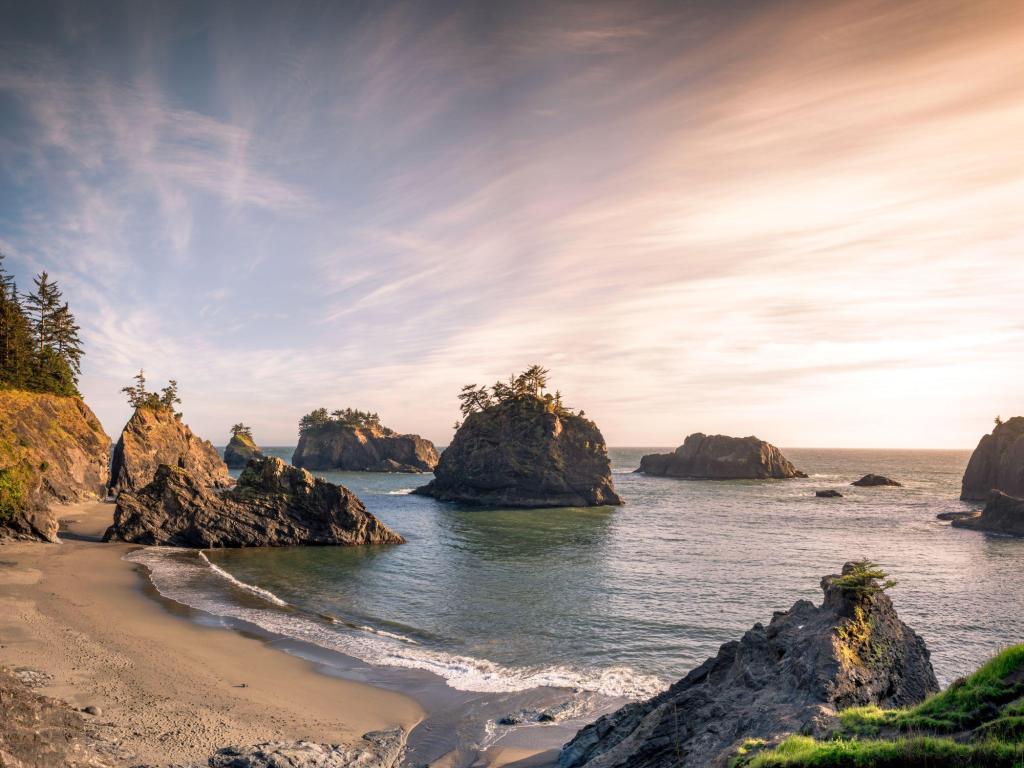 A sandy beach in a bay with rocks jutting out of the water.