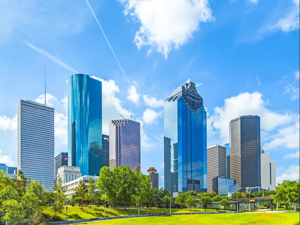 Houston, Texas, USA with the city skyline in daytime in the background and a green grass park in the foreground against a blue sky.