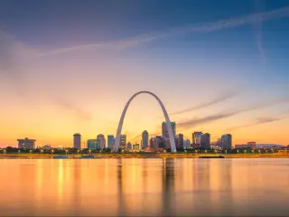 A sunset shot of the cityscape of St Louis with the famous arch in the foreground, overlooking water