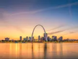 A sunset shot of the cityscape of St Louis with the famous arch in the foreground, overlooking water
