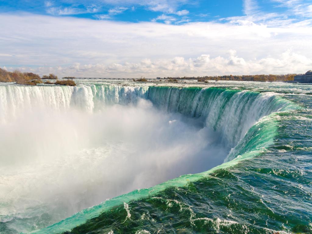 Massive horseshoe shaped waterfall with turquoise water at the top of the fall changing to white foam as it travels down the fall